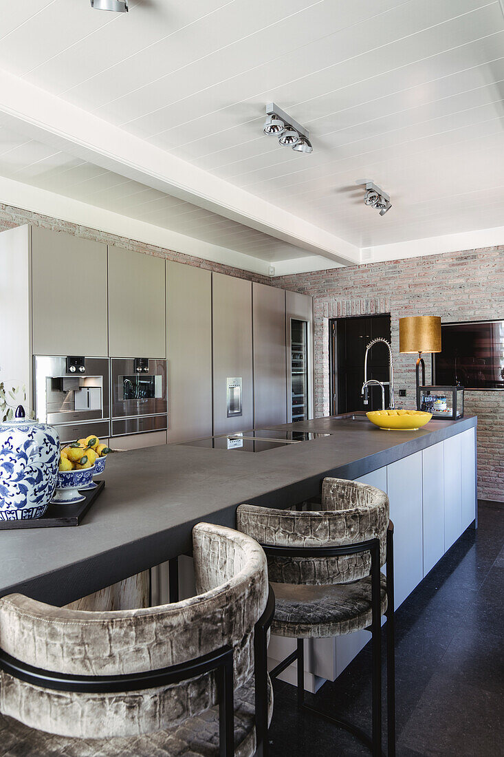 Modern kitchen with cooking island, bar stools and brick wall