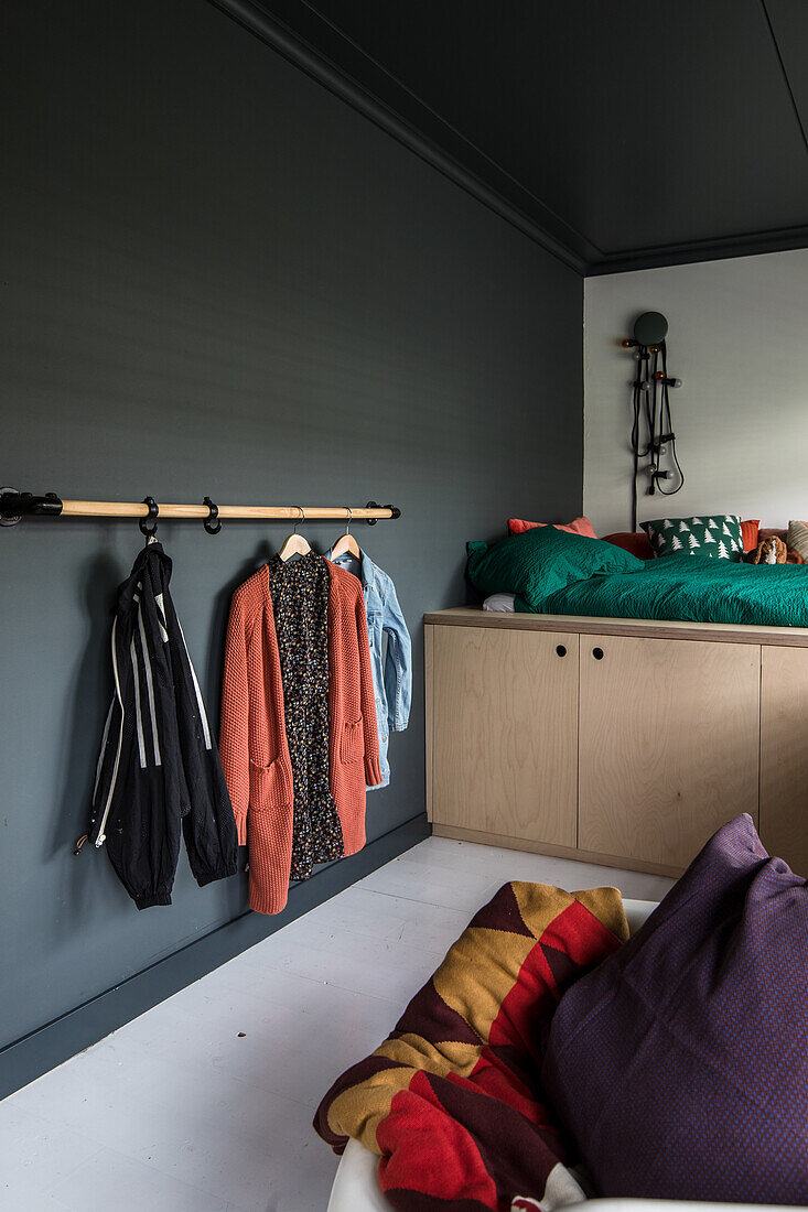 Bedroom with wall hooks for clothes, wooden chest of drawers and colourful cushions