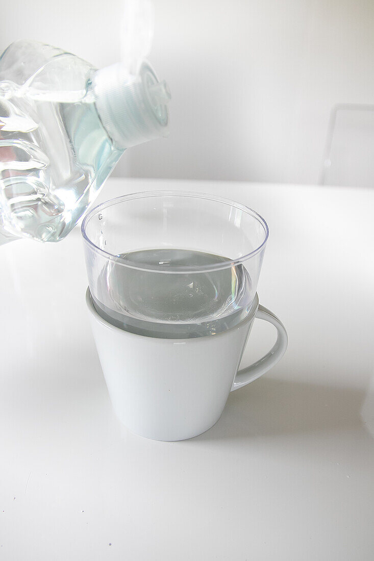 Wasser wird in eine durchsichtige Tasse über einer weißen Tasse gegossen