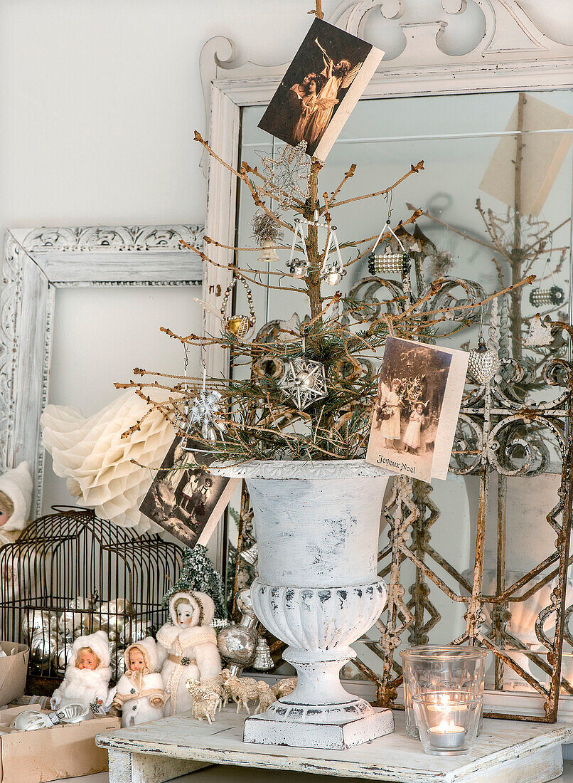 Kahler Weihnachtsbaum mit Weihnachtsschmuck und alten Karten in einer Urne, daneben Baumwollpuppen