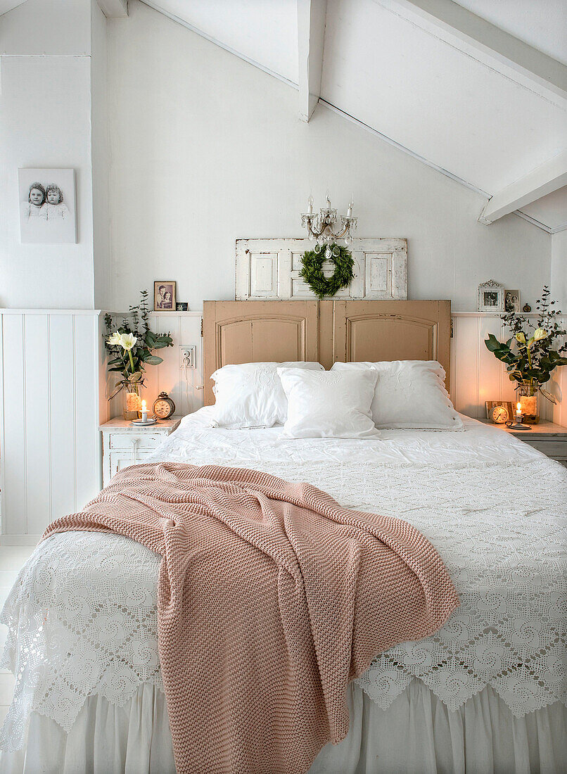 Double bed with white lace blanket, headboard made from old doors in a bedroom decorated for Christmas