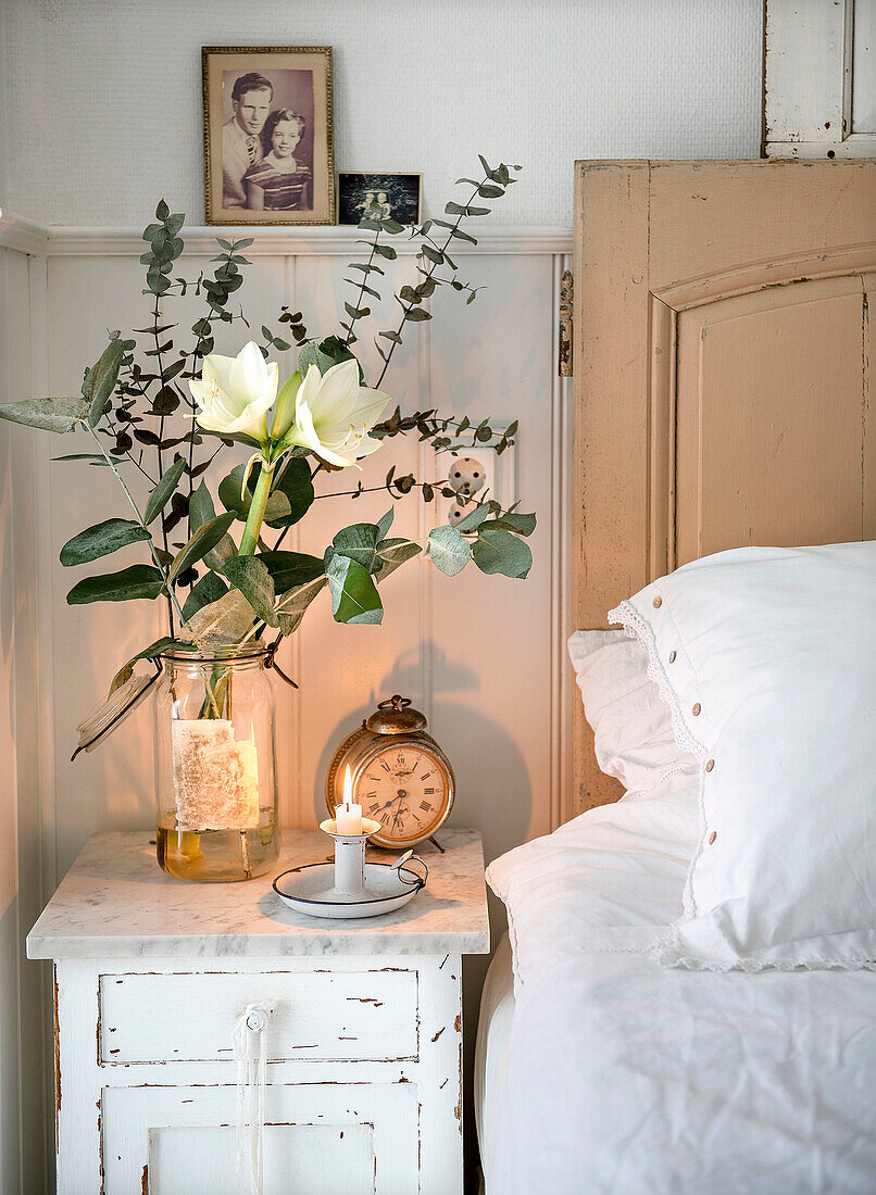 Weiße Amaryllis mit Eukalyptuszweigen auf altem Nachttisch neben dem Bett im Schlafzimmer