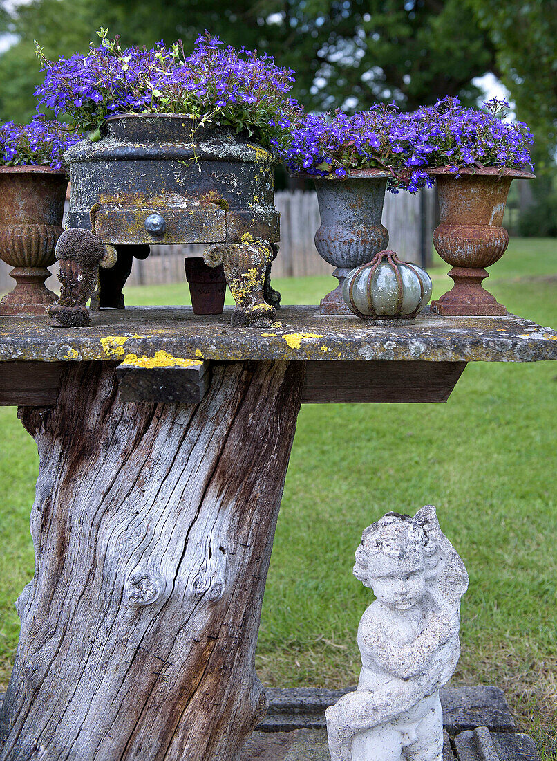 Rustikaler Gartentisch mit blühenden Lobelien und Steinfigur