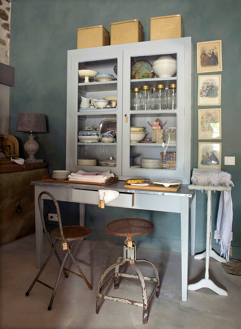 Display cabinet with crockery on table and vintage chairs