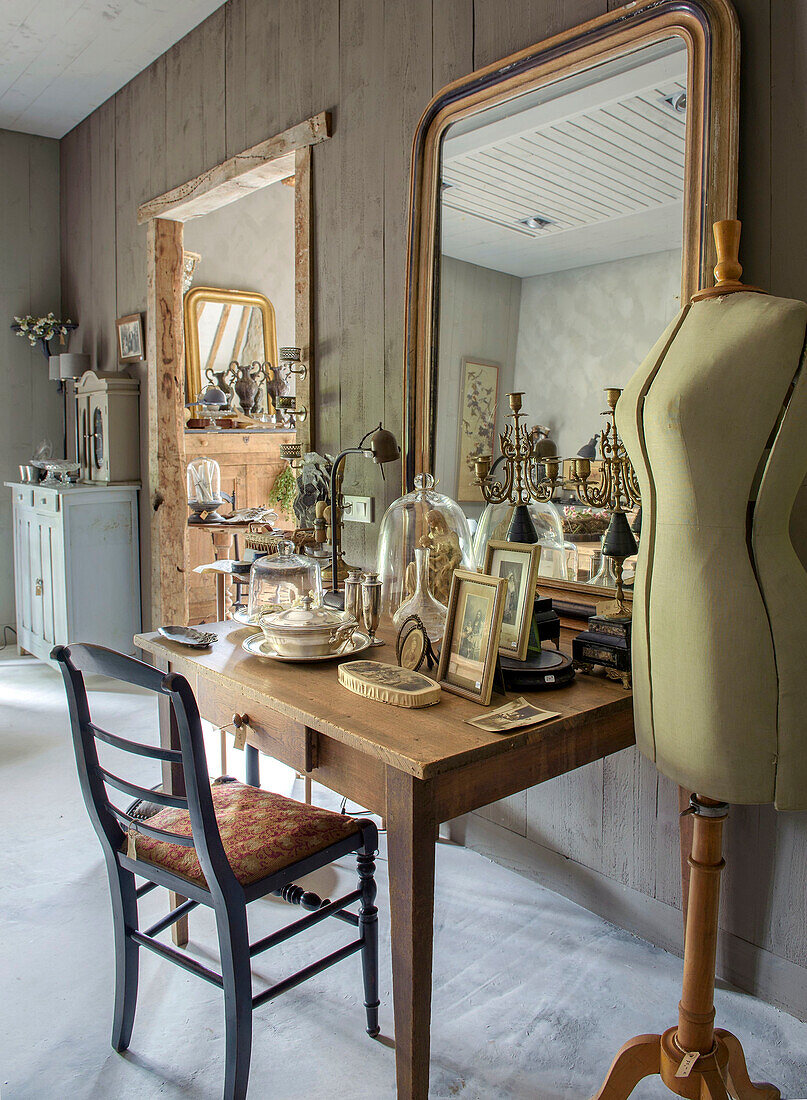 Wooden table with antique decorative objects and large mirror, with a dressmaker's dummy next to it