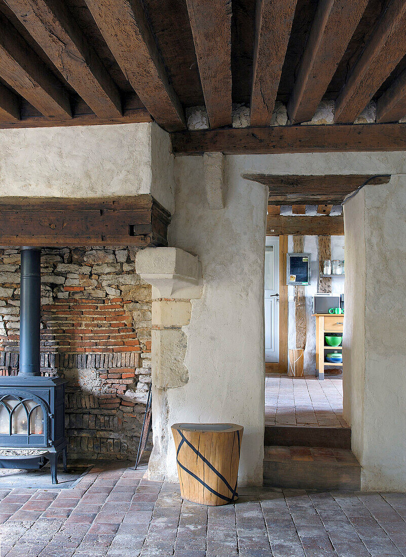 Wood-burning stove in front of brick wall in rustic room with wooden beam ceiling