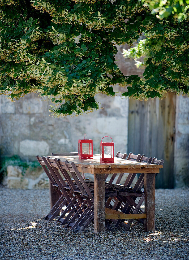Rustic wooden table with lanterns and folding chairs on gravel terrace