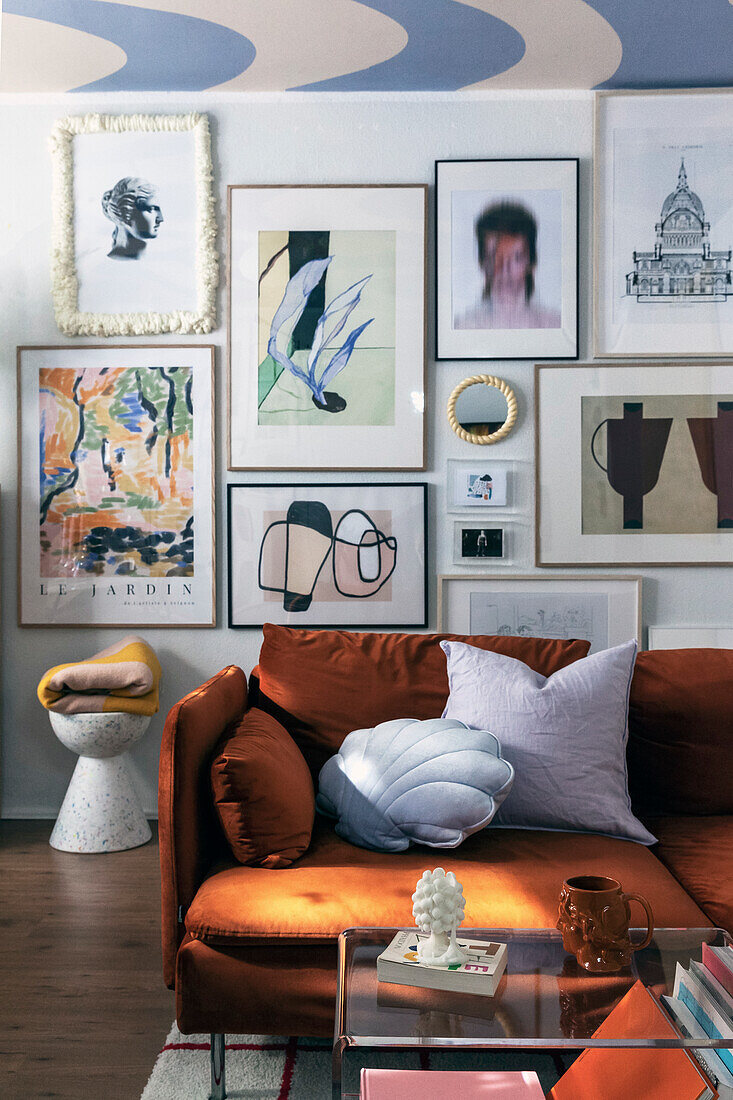 Picture wall in living room with orange-brown sofa and shell-shaped pillow