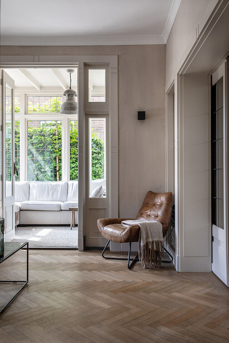 Hallway with herringbone parquet flooring, leather chair and view into the conservatory