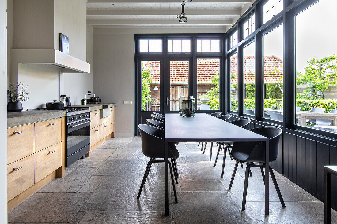 Moderne Küche mit langem Esstisch, schwarzen Stühlen und Blick in den Garten