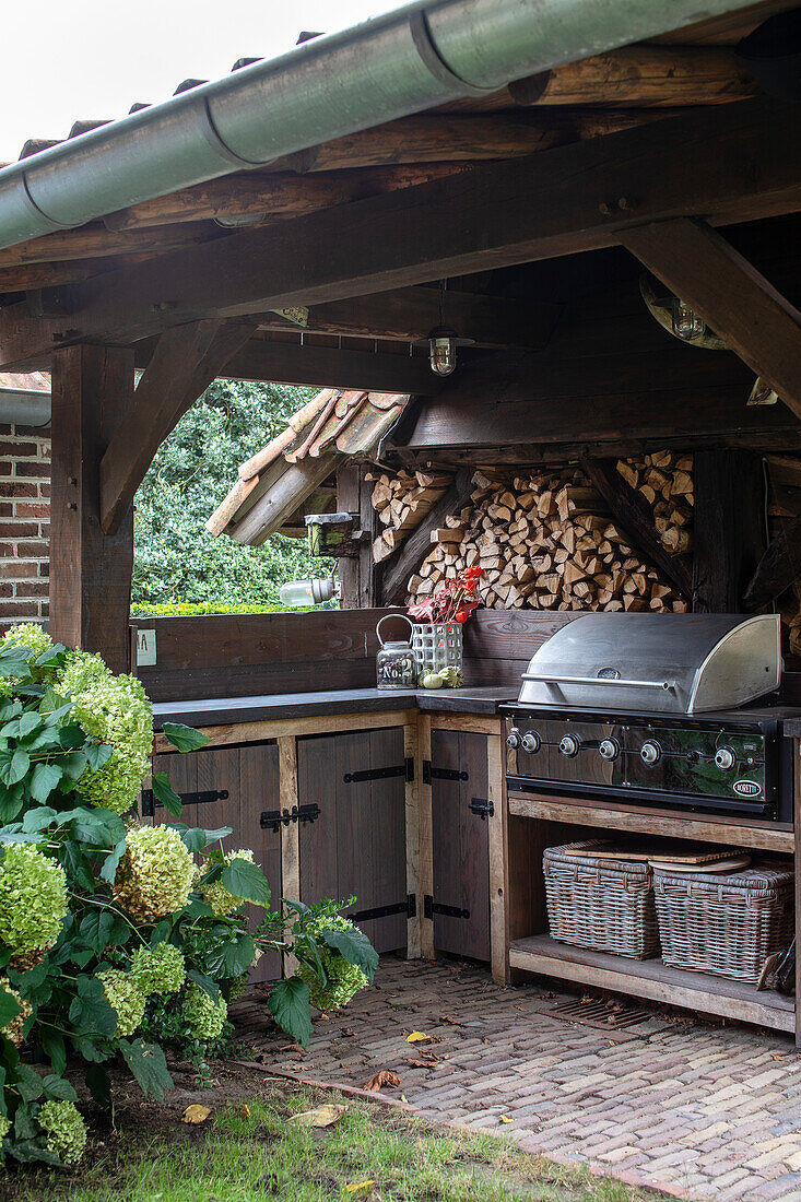 Überdachte Außenküche mit Grill und Brennholzlagerung im Garten