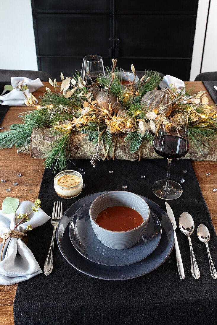 Festively laid wooden table with soup, dessert and winter decorations