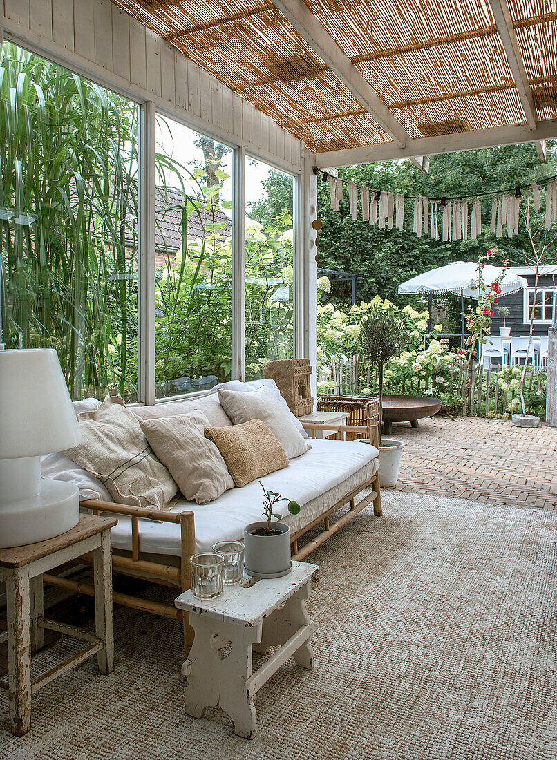 Covered terrace with bamboo sofa, throw pillows and plants in the background