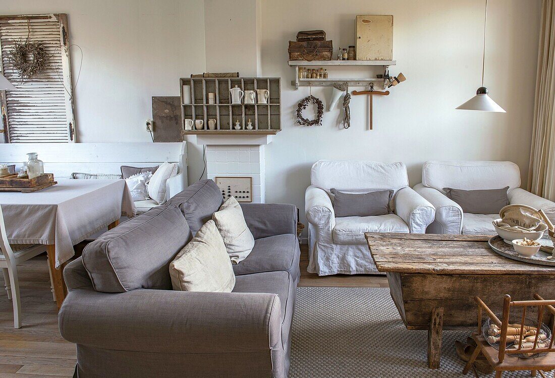 Country-style living room with white armchairs and grey sofa, rustic wooden table and decorative objects