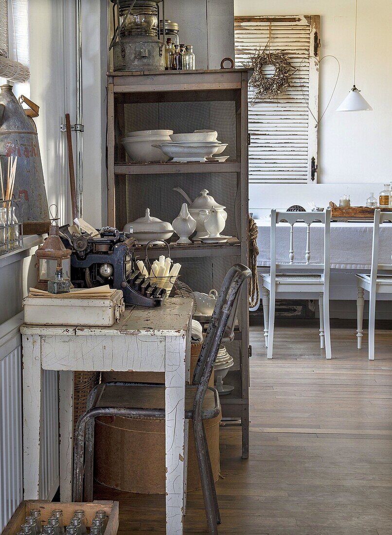 Vintage-Schreibtisch mit alter Schreibmaschine und Regal mit weißem Porzellan im Landhausstil