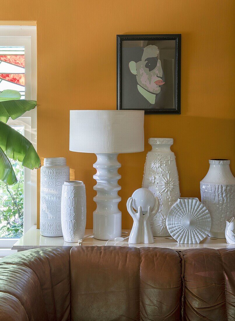 Vases and sculptures in white on console in front of yellow wall