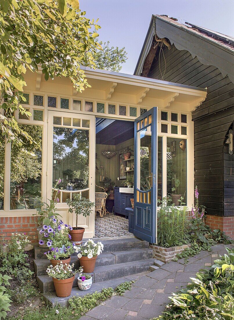 Conservatory with open door, stone staircase and flowering potted plants