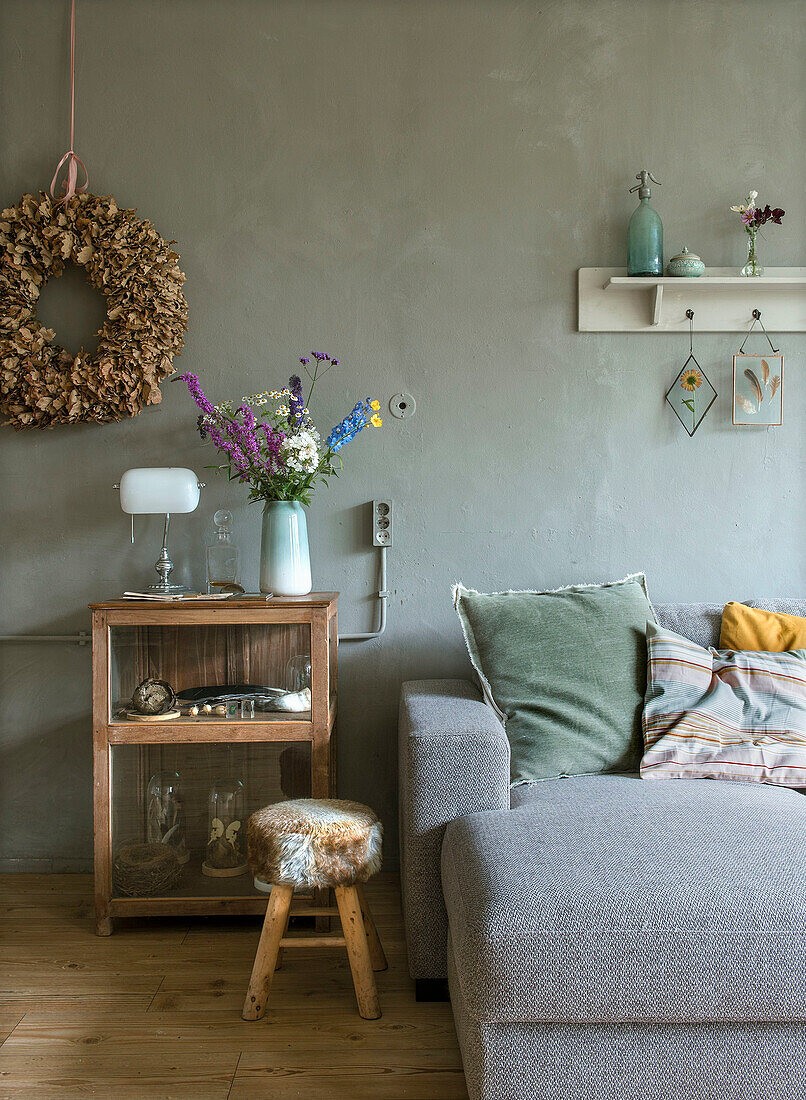 Grau gestrichene Wohnzimmerwand mit Blumenkranz, Hocker und rustikaler Holzschrank