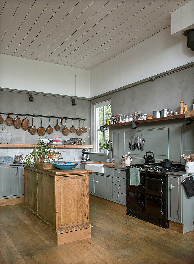 Country kitchen with wooden kitchen island, black oven and copper pans on the wall