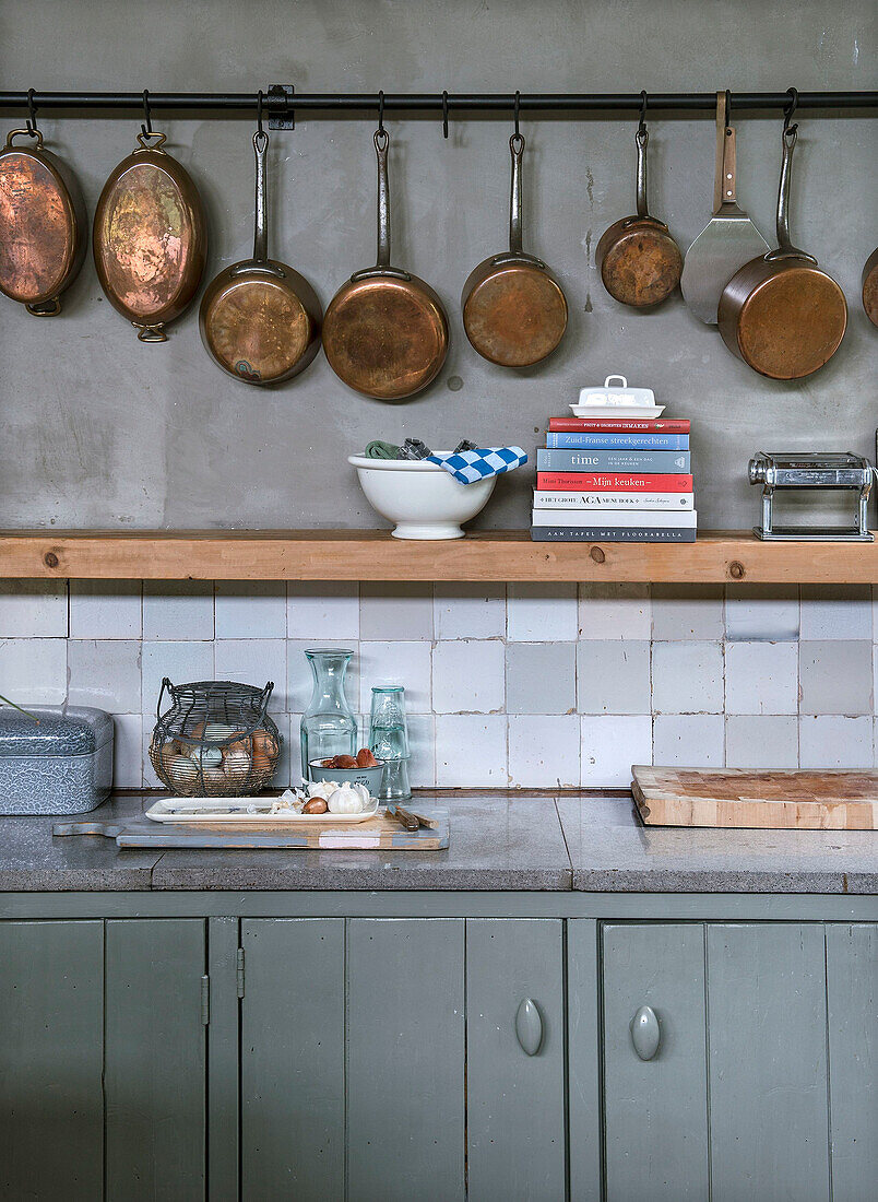 Copper pans on hooks in rustic kitchen with grey cupboards and wooden shelf