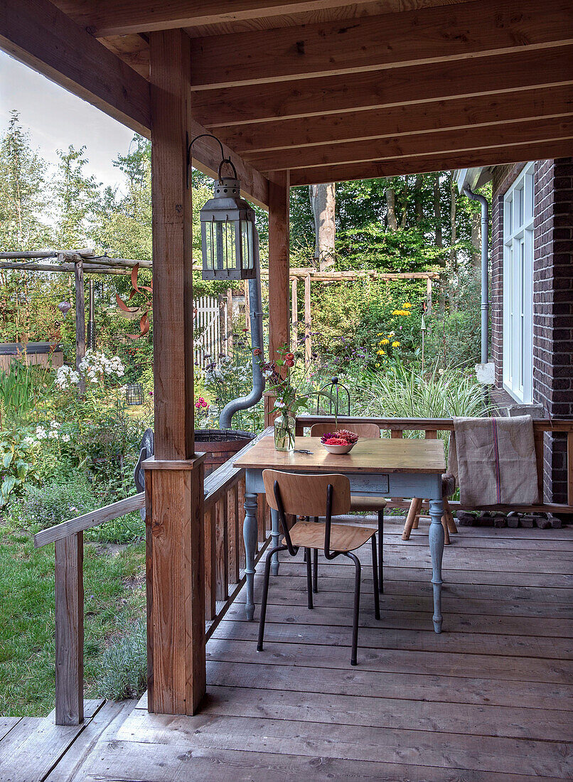 Holzveranda mit Tisch und Stühlen, Blick auf Garten im Sommer