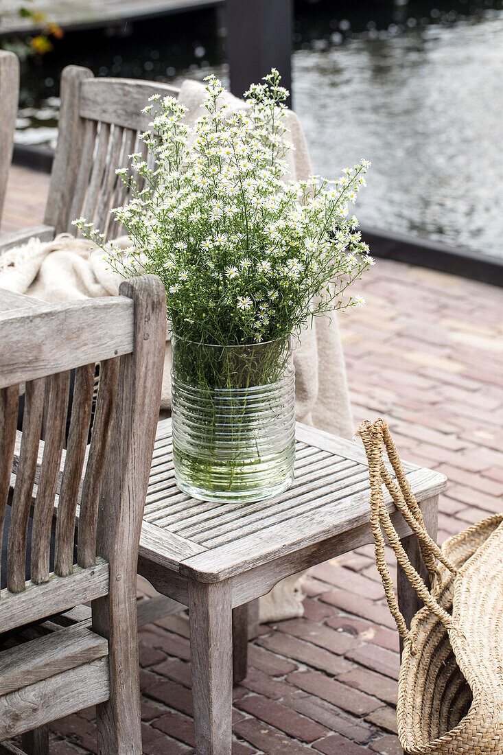 Glassvase mit weißen Blumen auf Holztisch im Freien