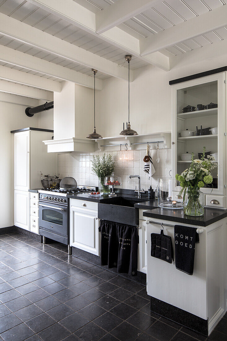 Country kitchen in black and white with tiled floor and wooden beamed ceiling