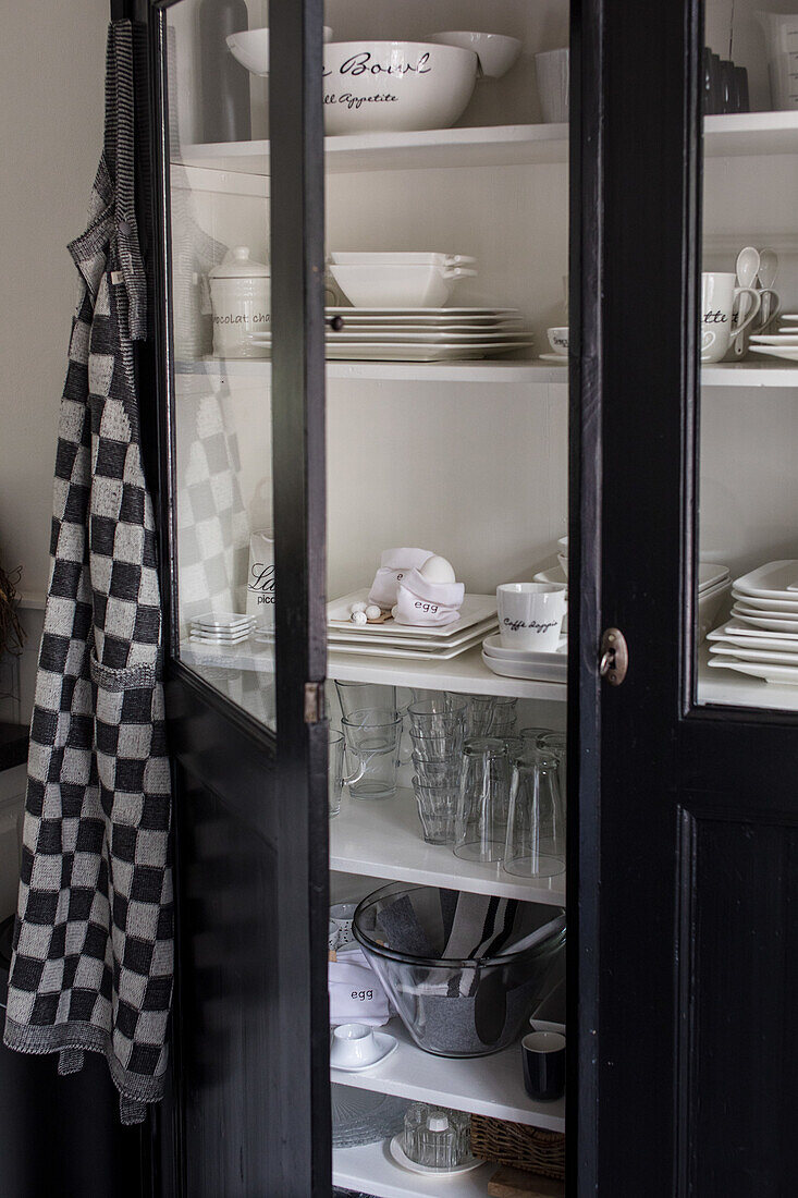 Black display cabinet with crockery, checkered apron