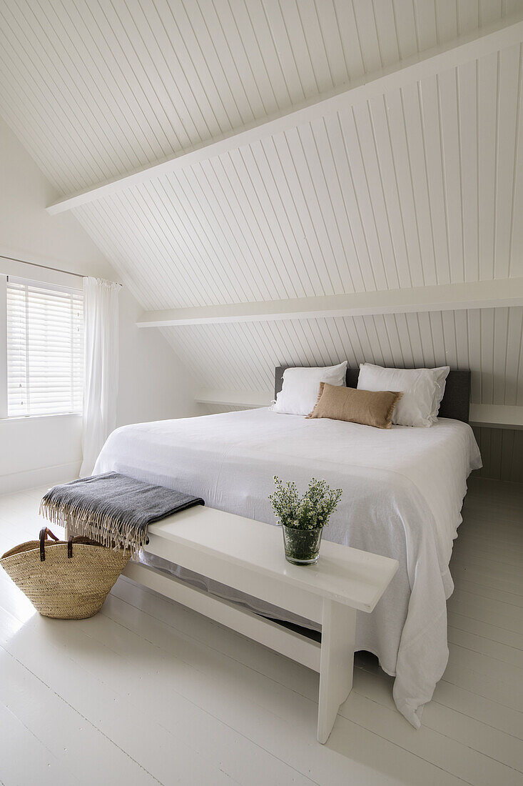 Bedroom in white with basket and bench at the end of the bed, sloping ceiling