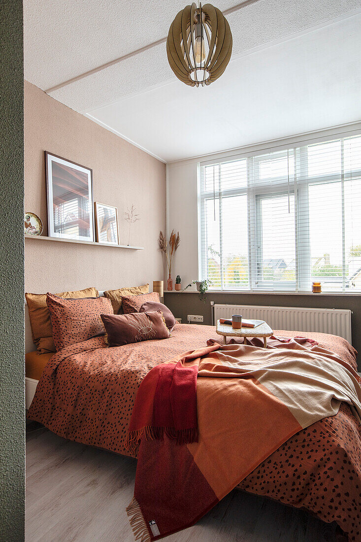 Bed with terracotta-coloured throw and cushions in modern bedroom