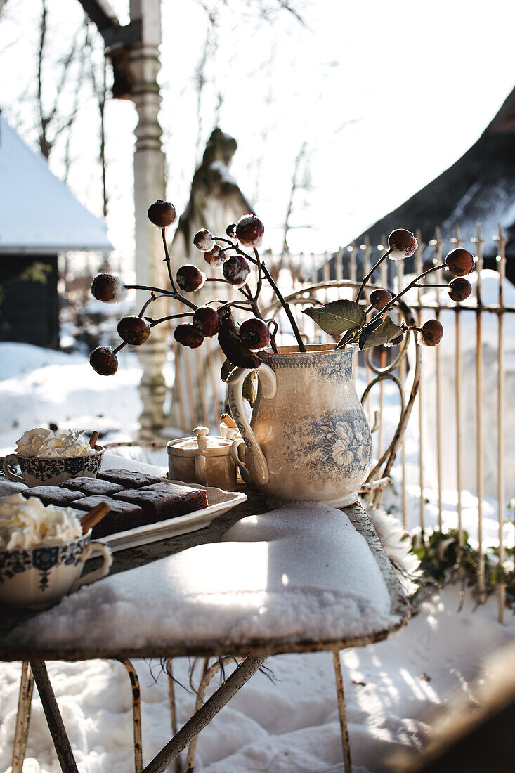 Winterlicher Gartentisch mit Keramikvase und Gebäck im Schnee