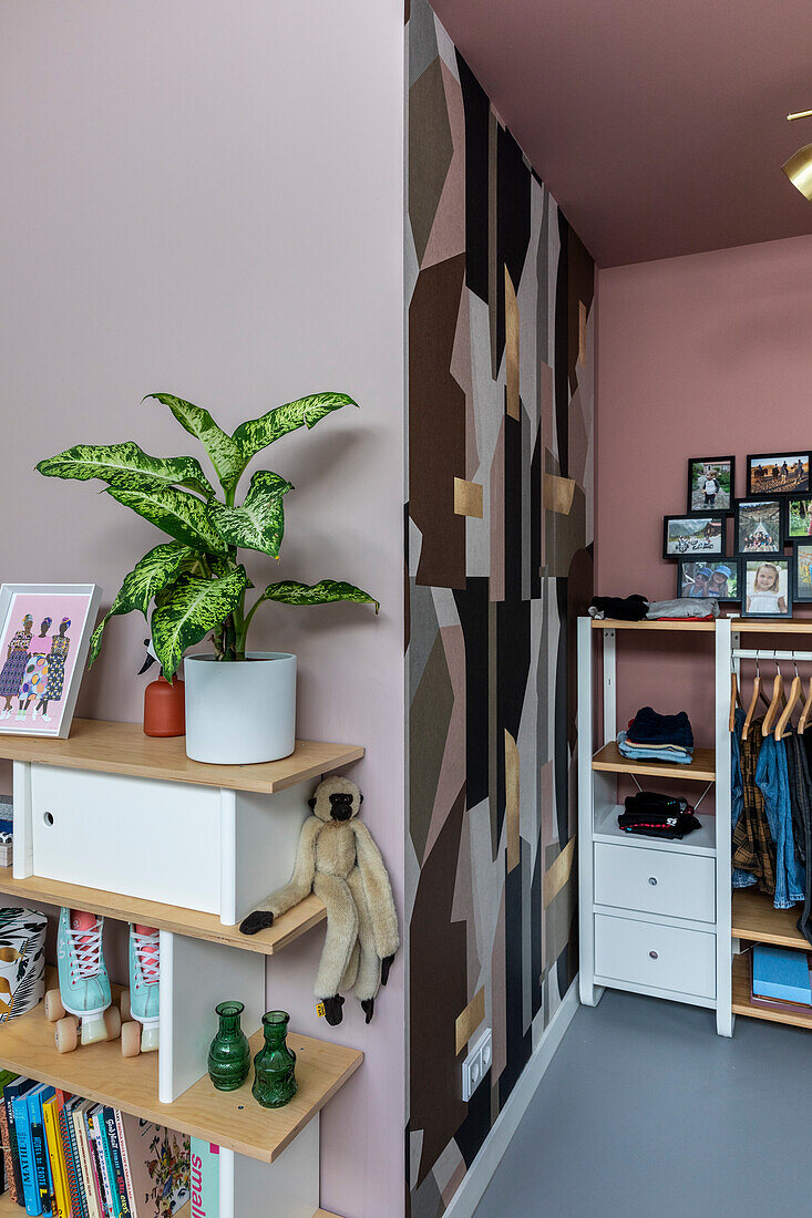 Open shelf with houseplant, books and decorations, patterned wall and open wardrobe