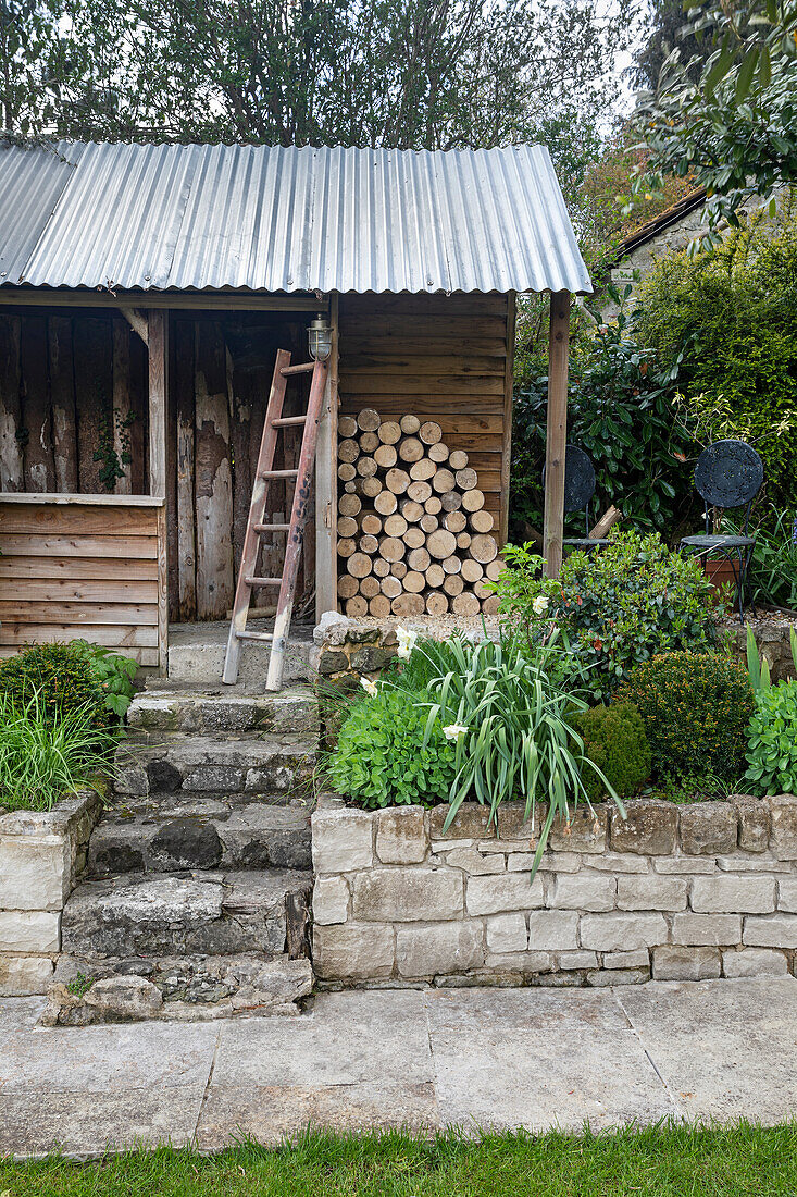 Beete mit Zierpflanzen und Feuerholzlager vor Gartenhütte