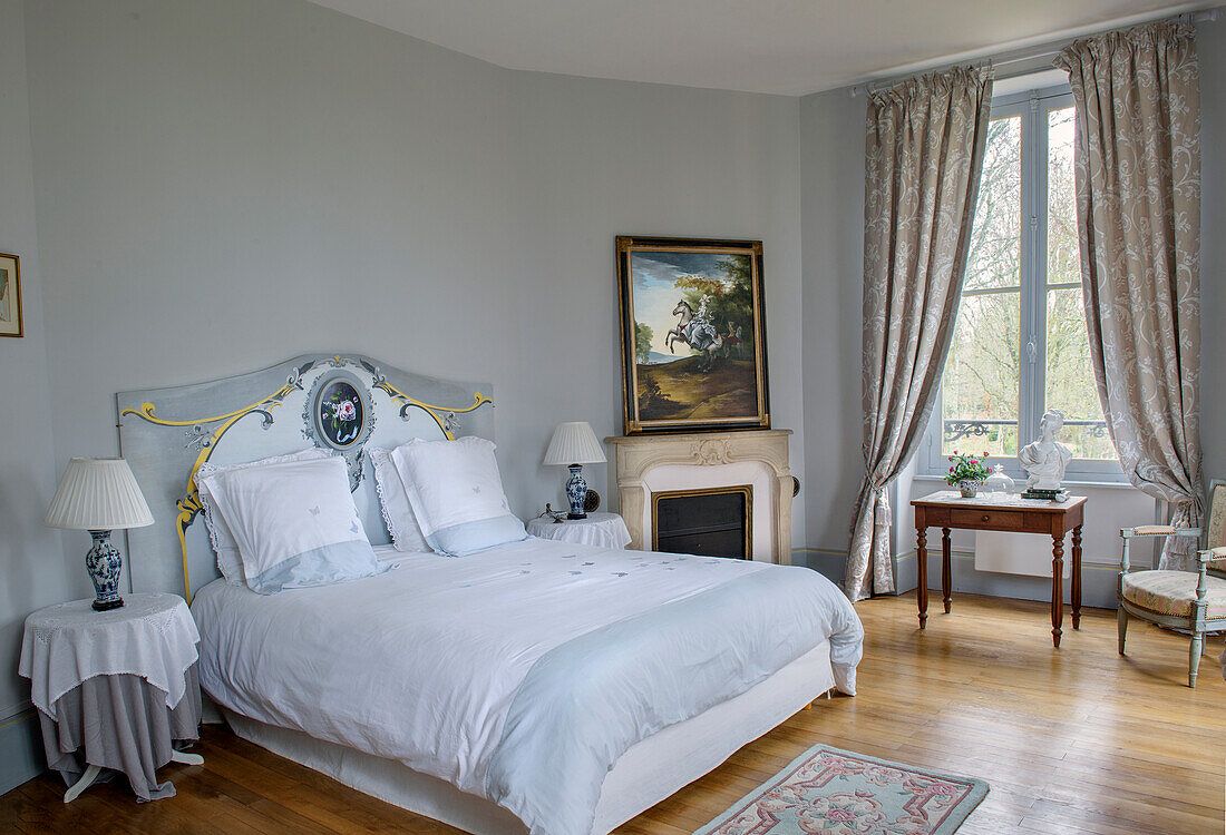 Double bed with ornate headboard next to the fireplace in the bedroom in soft blue tones