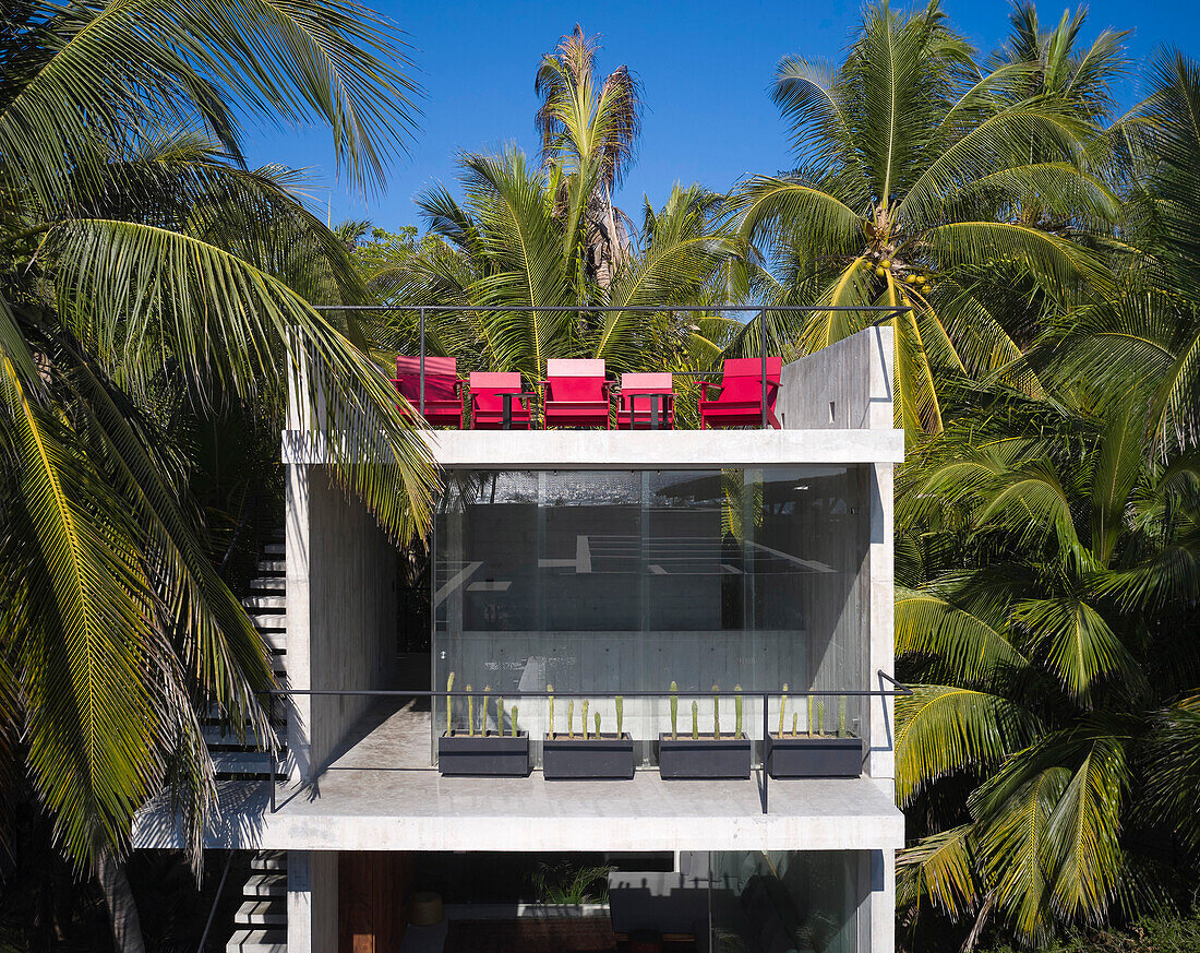 Front View of concrete beach house with balcony and roof terrace between palm trees