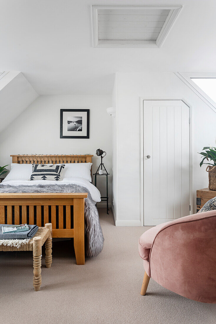 Schlafzimmer mit Holzbett, rosa Sessel und weißen Wänden