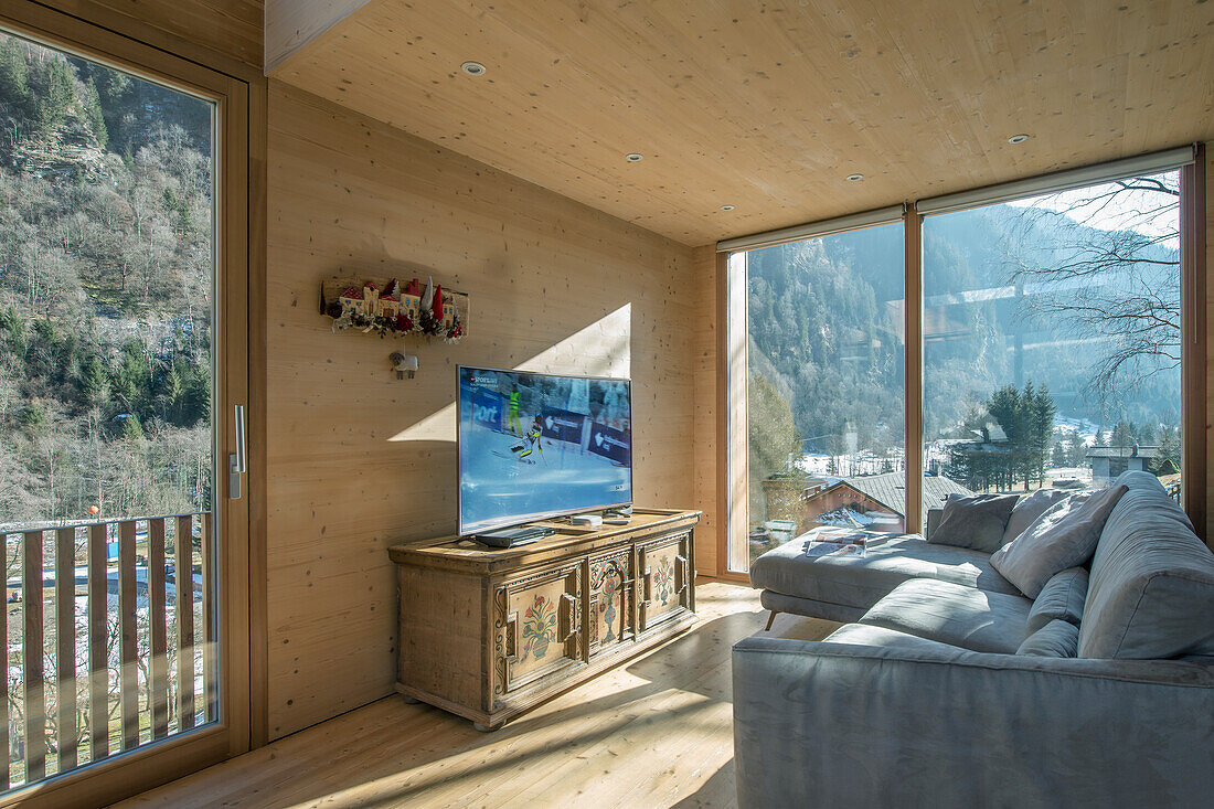 Living room with panoramic windows, grey sofa and rustic wooden TV stand