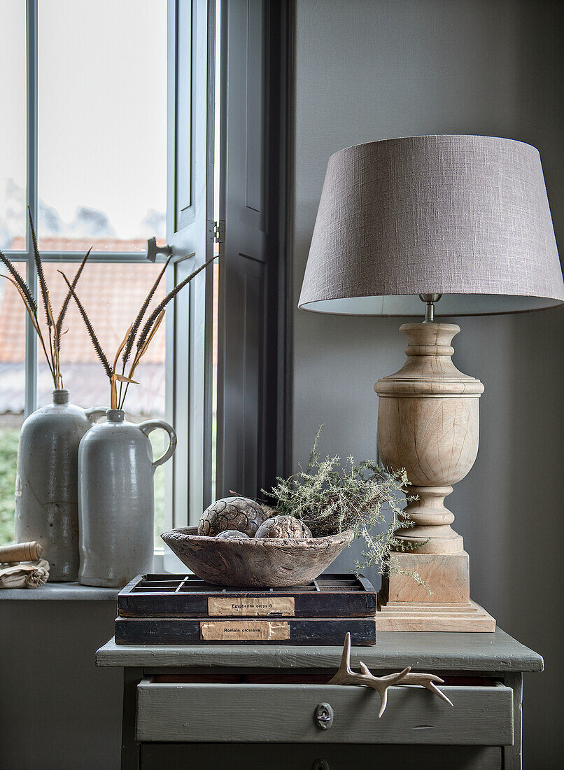 Lampe, Trockenblumen und Deko-Objekte auf Tisch am Fenster