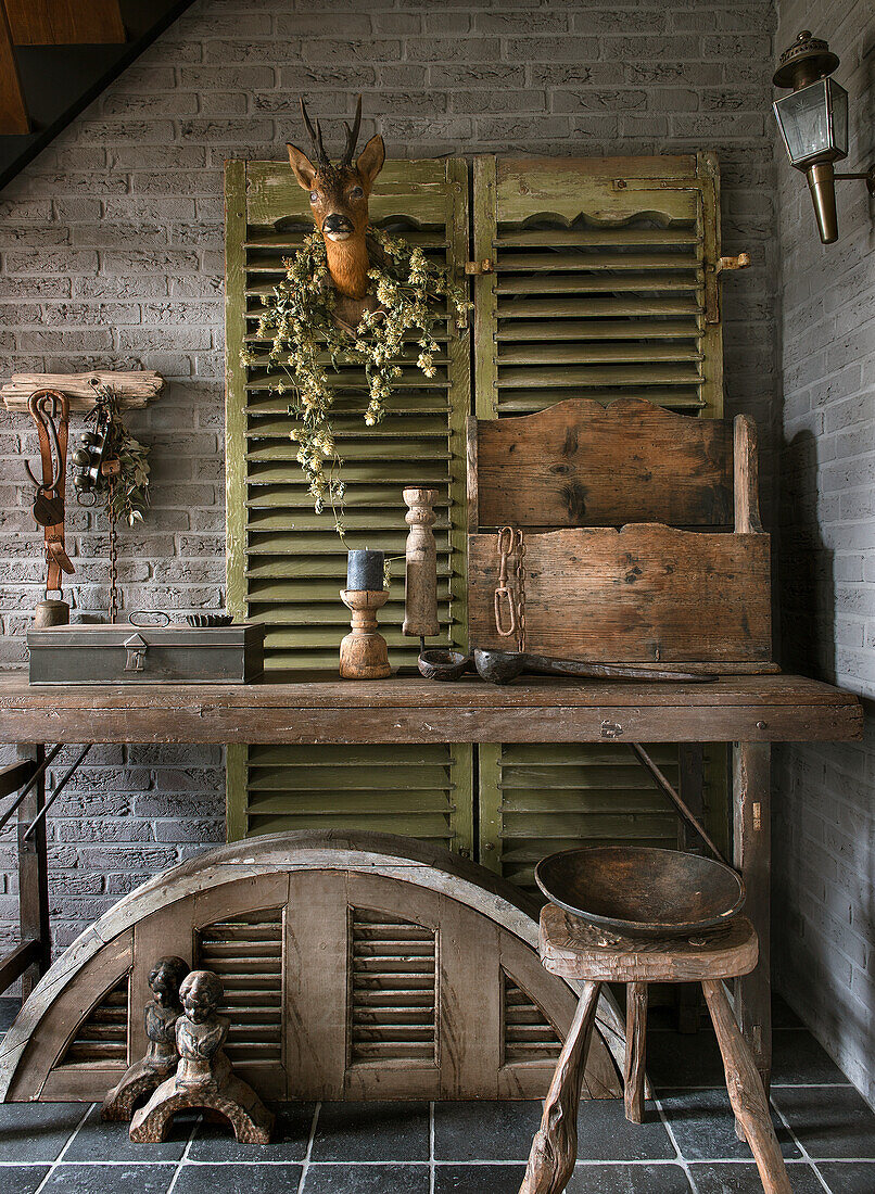 Rustic table, wooden box and shutters with louvres in front of brick wall