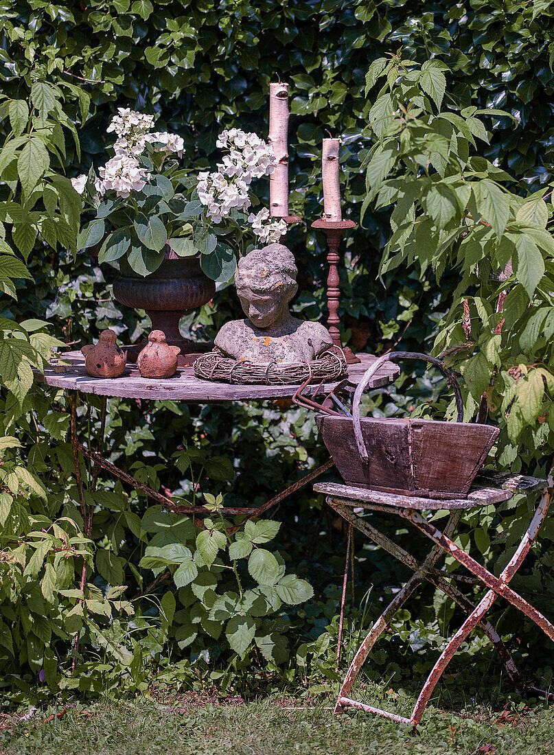 Rustikaler Gartentisch mit Kerzen, Statuette und weißen Hortensien