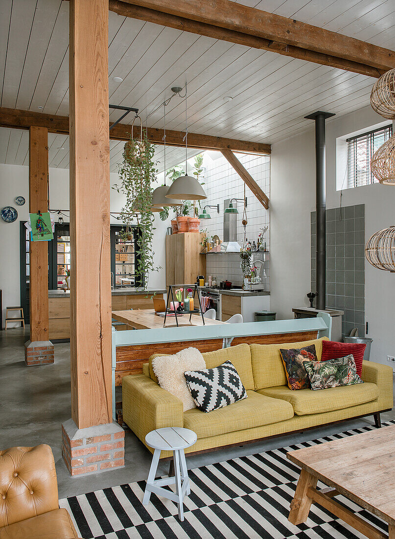 Open-plan living area with wooden beams, yellow sofa and striped carpet