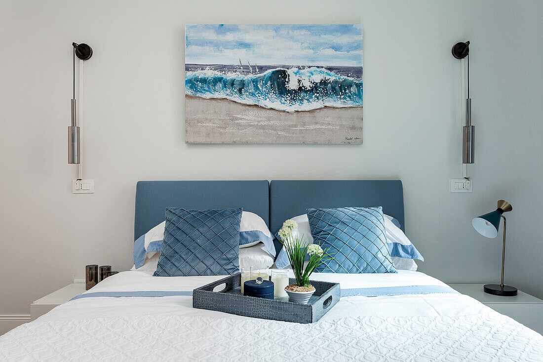 Bed with blue and white bed linen and seascape in modern bedroom