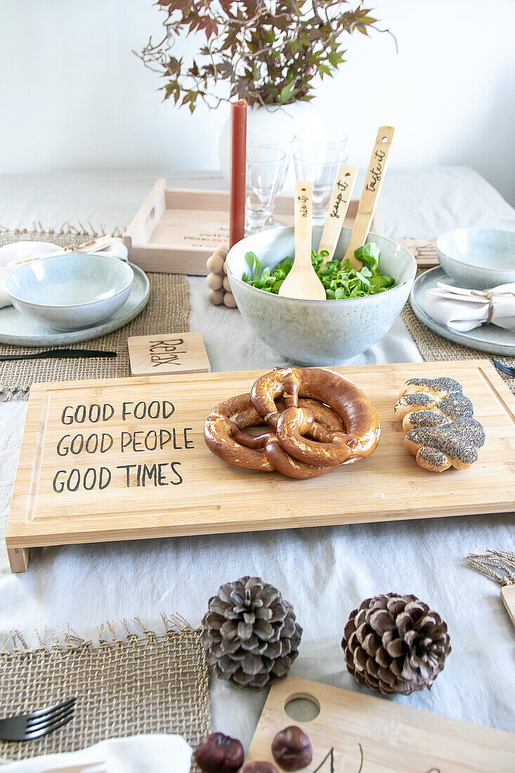 Gedeckter Tisch mit Brezeln auf DIY-Holzbrett und Salatschüssel