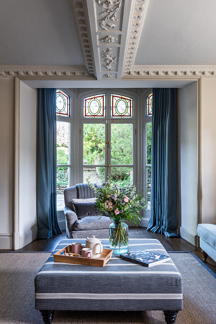 Living room with high windows, blue curtains and decorative mouldings on the ceiling