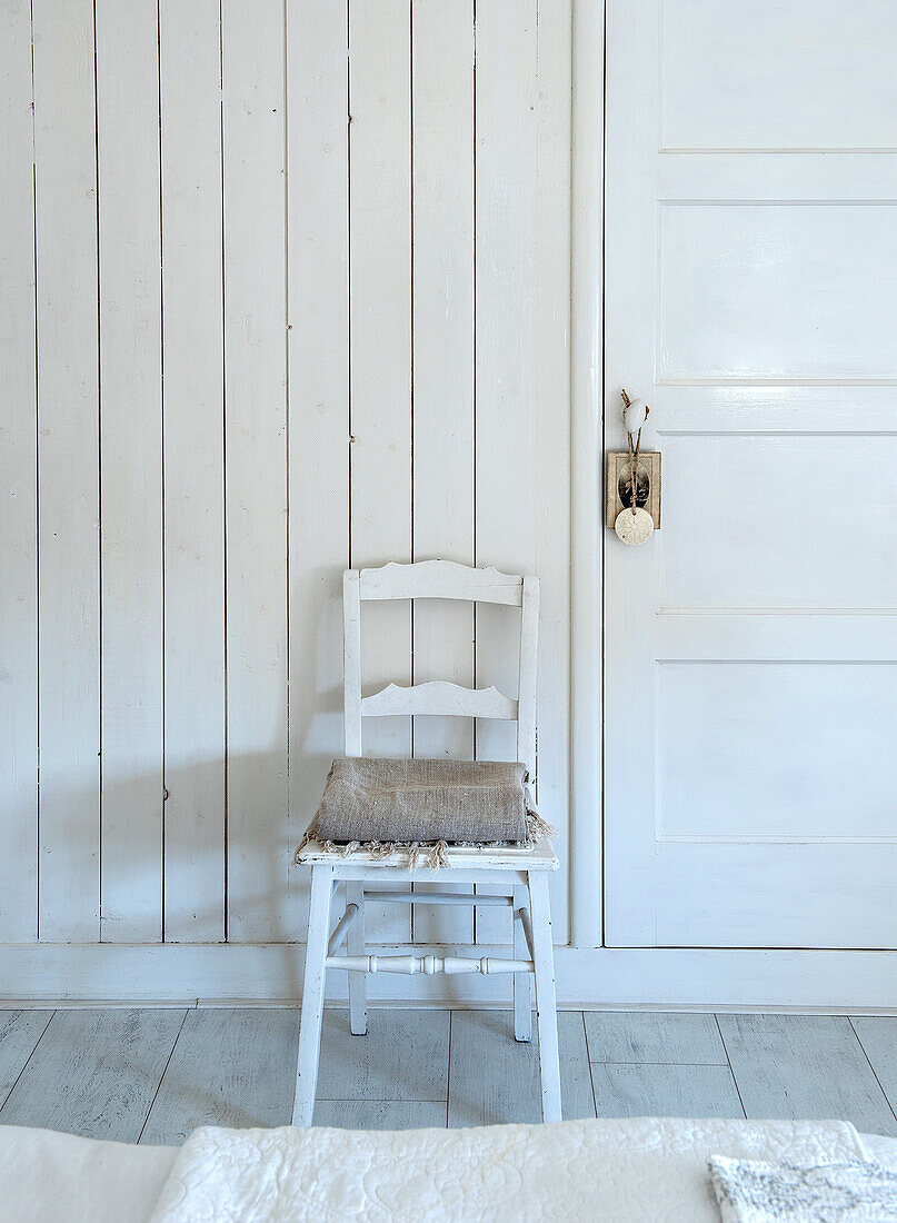 White-painted wooden chair with seat cushion in front of country-style wood paneling