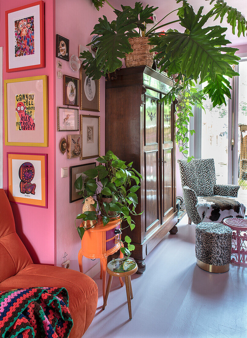 Living room designed in shades of pink with plants, orange vintage chest of drawers and wooden cabinet