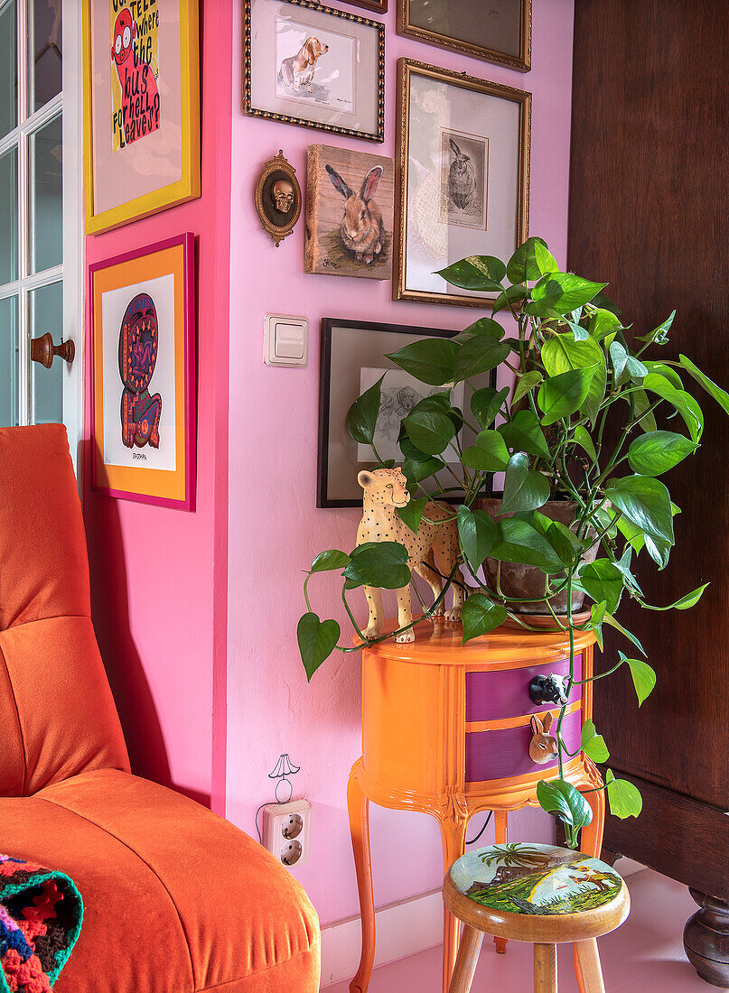 Orange side table with houseplant in front of colorful picture wall