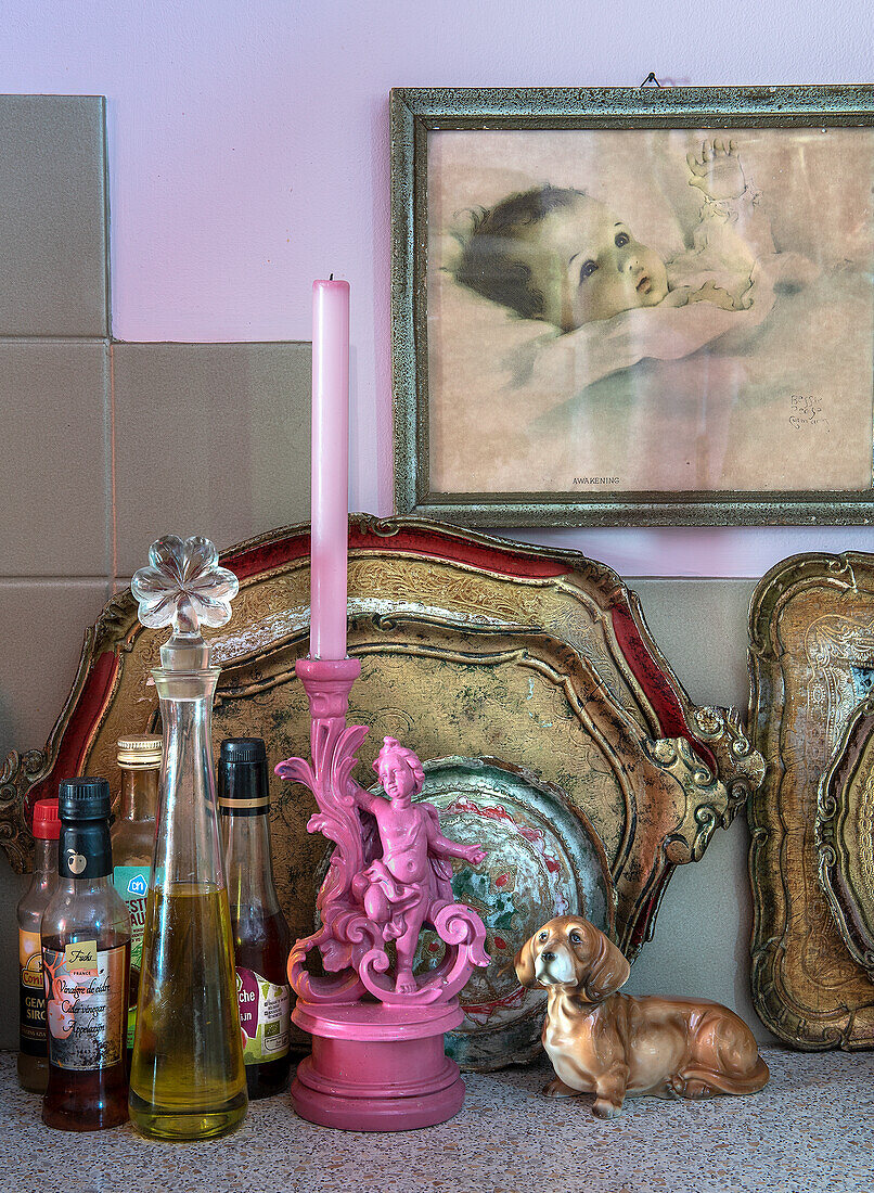 Pink candle holder with putto, vinegar and oil bottles, dachshund figurine and gold-decorated trays on kitchen worktop