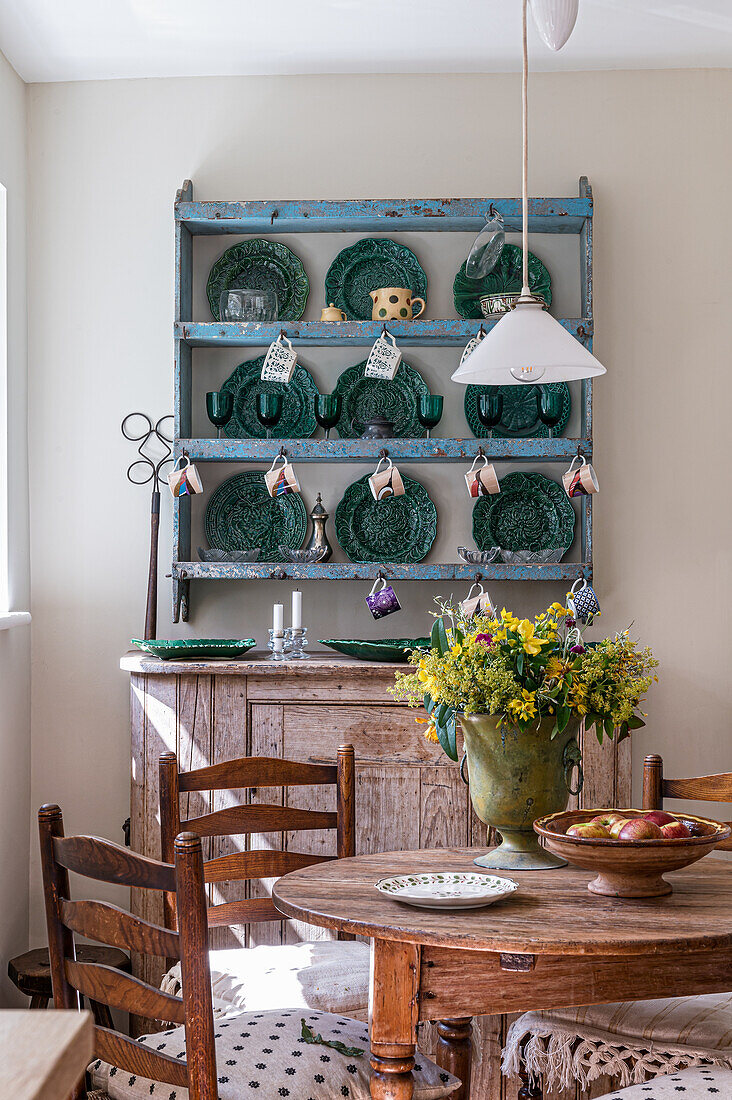 Dining room with rustic wooden table, chairs and green ceramic crockery on a wooden shelf