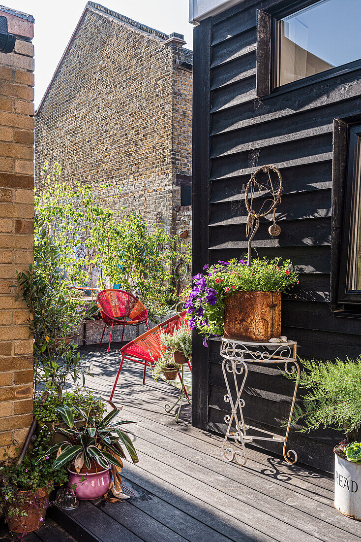 Wooden terrace with red chairs, flower pots and black wooden facade in the backyard